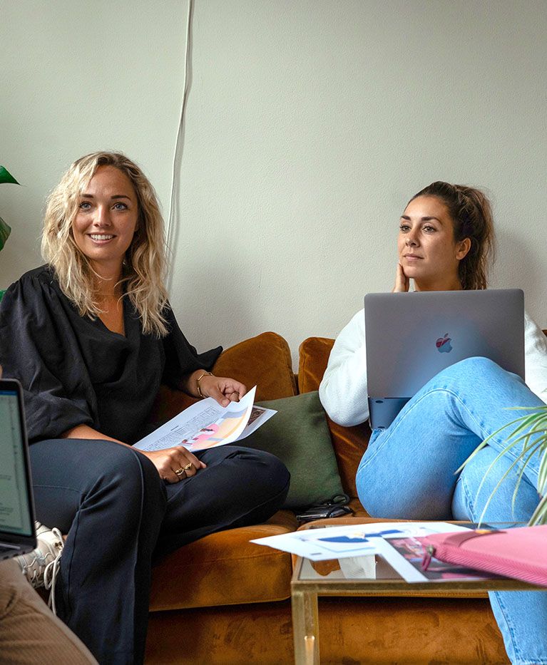 Three women chat around a table with laptops and a pink Case Logic laptop sleeve sits on the table.