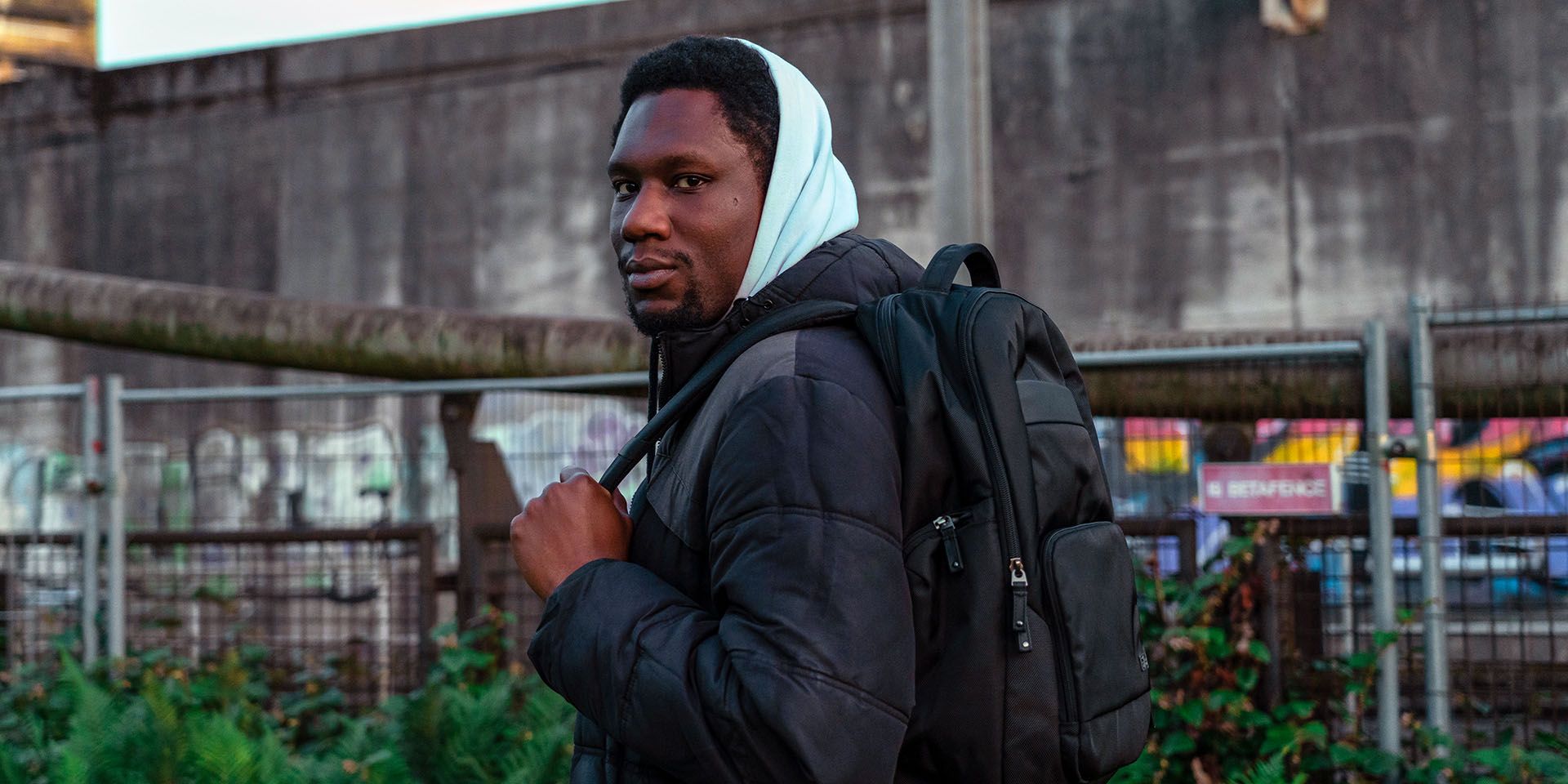 A man stands in a city environment with a black Case Logic backpack.
