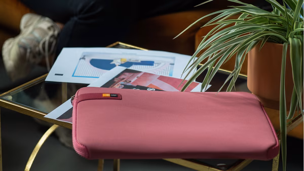 A pink Case Logic laptop sleeves sits on an end table next to some papers