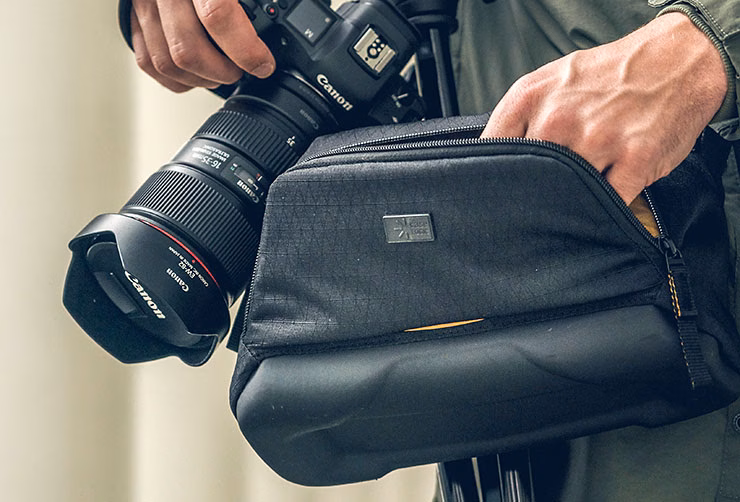A close-up of someone holding a camera and reaching into their Case Logic camera bag.