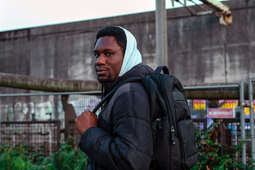 A man stands in a city environment with a black Case Logic backpack.