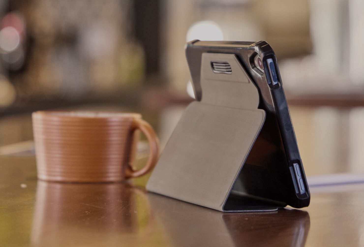 A close-up of a Case Logic tablet case holding up a tablet on a table with a coffee cup.