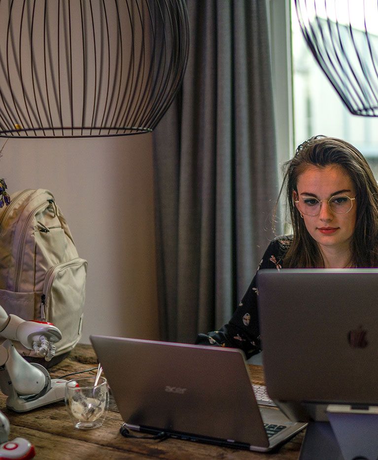 A students sits at a desk with her laptop, a small robot, and a Case Logic backpack.