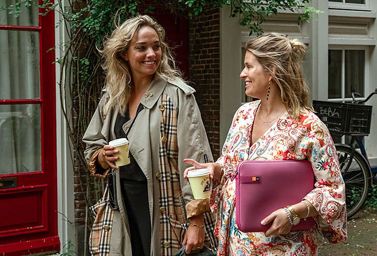 Two women walk down a street holding coffees and a Case Logic pink laptop sleeve.