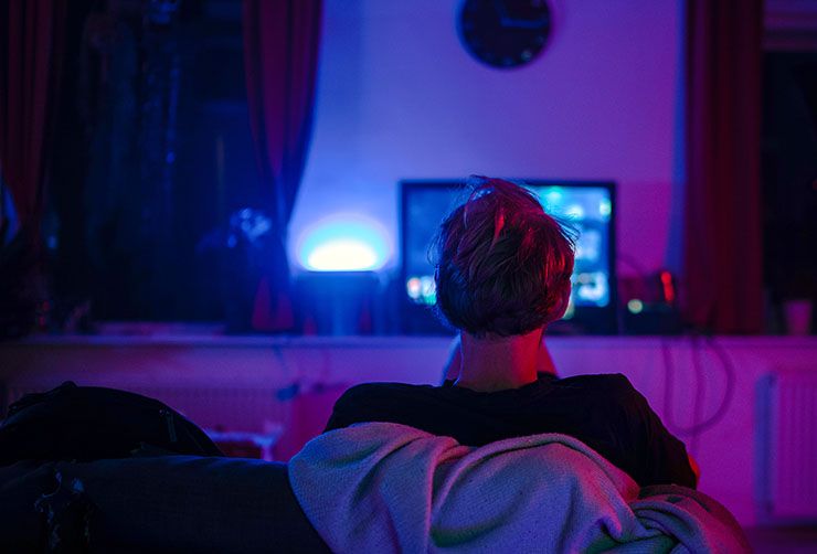 A man in the dark playing a computer game with his back to the camera.