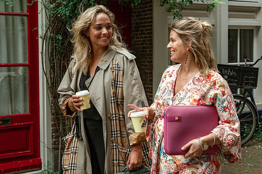 Two women walk down a street holding coffees and a Case Logic pink laptop sleeve.