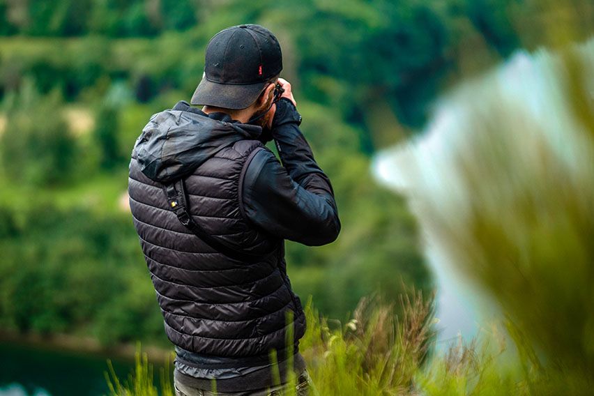 A man takes a picture of nature with a Case Logic camera shoulder bag around his shoulder.