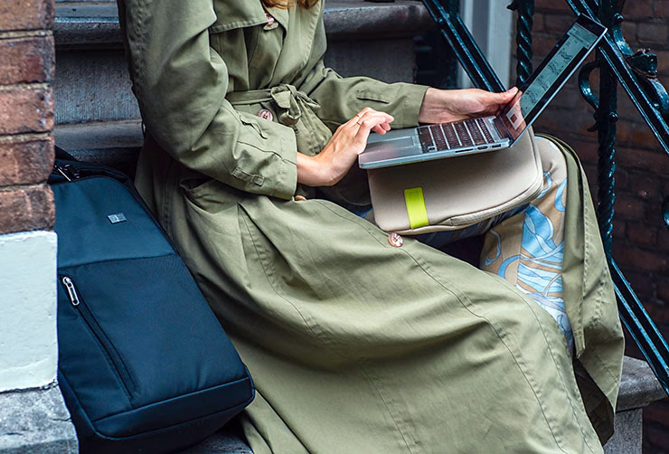A woman sits on a stoop looking at her computer with a Case Logic laptop backpack next to her.