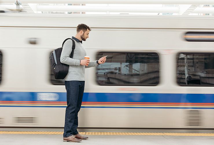 Man checks phone carrying a Case Logic Advantage backpack while waiting for a train,